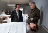Donna Leon – Der Gerichtsmediziner Dottor Aurino (Ueli Jäggi, re.) erklärt Commissario Brunetti (Uwe Kockisch), dass Signora Altavilla (Roswitha Dierck) keines natürlichen Todes starb – obwohl im Totenschein Herzversagen angegeben wurde.