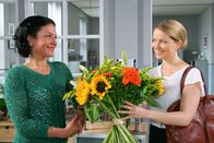 Die Rosenheim-Cops – Noch glaubt Controllerin Ortmann (Diana Staehly, r.), dass der Blumenstrauß für sie bestimmt ist. Sekretärin Stockl (Marisa Burger, l.) freut sich mit ihr.