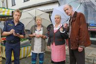 Die Rosenheim-Cops – Polizist Mohr (Max Müller, l.) befragt die Standbetreiber Marianne Widl (Erika Fischer-Laughlin, 2.v.l.), Gertie Pointner (Johanna Bittenbinder, 2.v.r.) und (Werner Kraisig (Johannes Herrschmann, r.), die ebenfalls am Markt ihre Waren verkaufen.