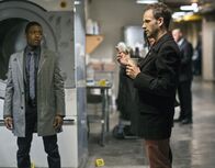 Elementary – Die Leiche des Geschäftsführers eines Nobelhotels in Manhattan wurde in einer Industriewaschmaschine gefunden. Sherlock Holmes (Jonny Lee Miller, r.) und Marcus (Jon Michael Hill, l.) sehen sich den Tatort an, um den Täter zu überführen ...