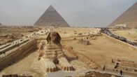 Universum History – Die Sphinx-Statue von Gizeh vor einer der Pyramiden von Gizeh.