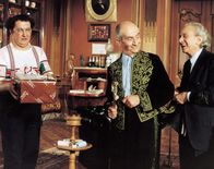 Brust oder Keule – Während Charles (Louis de Funès, m.) mit seinem privaten Schneider (Marcel Dalio, r.) scherzt, versucht Gérard (Coluche, l.) seiner Angebeteten Marguerite mit einem Präsent zu schmeicheln.