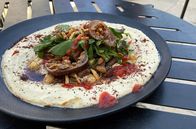 Stadt Land Kunst – Fadis israelischer Hummus besteht aus einer klassischen Basis aus Kichererbsen, Knoblauch, Tahina, Zitronensaft und Kumin. Dann bedeckt er das Ganze mit Lammfleisch, Pinienkernen, Mandeln, gefüllten Auberginen und Kräutern.