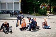 neoriginal: Aufgestaut – Die Polizei macht sich an die Arbeit: Während Strasser (Altine Emini, 2.v.l.) die genaue Position der Protestierenden markiert, prüft ihr Kollege Wuttke (Daniel Donskoy, M.), ob er Lenas (Valerie Stoll, 3.v.l.) Hand gewaltfrei vom Asphalt lösen kann. Doch da ist nichts zu machen - Lenas Hand klebt fest!
