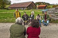 Falsche Siebziger – An der Bushaltestelle in Gelting probt man eine Alttagssituation, damit die falschen Darsteller sich in ihre Rollen finden. von links: Kathrin von Steinburg (Iris Schranner), Gerhard Wittmann (Karl Kainz), Ilse Neubauer (Kath Kainz / Marlies Braun), Markus Krojer (Daniel Hochstetter), Sebastian Bezzel (Hubertus Hochstetter); mit dem Rücken zugewandt: Fred Stillkrauth (Cajetan Hochstetter / Johannes Tiefenbach), Gundi Ellert (Falsche Anna / Vevi Schlattner)