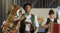 Watzmann ermittelt – Der Flüchtling Alfons Nkmura (Dimitri Abold, M. mit Komparsen), genannt Fonsi darf die Goaßlschnalzer in den prestigeträchtigen Wettkampf führen.