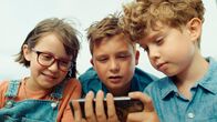 Geschichten vom Franz – Drei Kinder sitzen nebeneinander und schauen gemeinsam auf ein Smartphone.