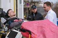 In aller Freundschaft – Der wegen Totschlag verurteilte Dennis Karow (Ilja Roßbander, li.) hat sich bei einem Fluchtversuch aus der JVA schwer verletzt. In Begleitung eines Polizisten (Komparse, mi.) wird er in der Sachsenklinik an Dr. Kai Hoffmann (Julian Weigend, re.) übergeben.