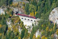 alpha-expedition: Mit dem Zug ... – Roter Zug auf einem Viadukt zwischen zwei Tunneln der Semmeringbahn. Die Semmeringbahn ist die älteste Bergbahn Europas und Weltkulturerbe der Unesco.