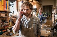 Watzmann ermittelt – Schreinermeister Sebald Wimmer (Andreas Nickl, l.) telefoniert im Beisein seines Sohnes Moritz (Lorenzo Nedis Walcher, r.) mit seiner der Bank.