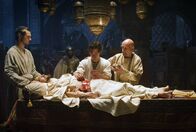 Der Medicus – Unter Mithilfe seines Meisters Ibn Sina (Ben Kingsley, rechts) und seinem Mitstudenten Mirdin (Michael Marcus, links) führt Rob (Tom Payne, Mitte) bei dem erkrankten Schah (Oliver Martinez) eine Blinddarmoperation durch.