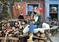Rabe Rudi - Vorlese-Geschichten – Milena Tscharntke und Rabe Rudi sitzen auf einem Holzstapel und schauen freundlich in die Kamera.