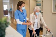 ATV - Die Reportage – Smiling nurse with face mask helping senior woman to walk around the nursing home with walker.