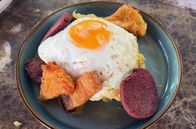 Stadt Land Kunst – In Las Terrenas bereitet Marian ein traditionelles Frühstück zu. Es besteht aus Kochbananenpüree, das mit Speck, gebratenem Käse, Salami, Würstchen, Avocado, Zwiebeln und Eiern serviert wird.