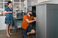 Die Rosenheim-Cops – Paketbote Hannes Winkler (Steffen Wolf, r.) versucht, den Aktenschrank im Büro von Miriam Stockl (Marisa Burger, l.) zu reparieren.