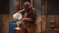 Moonshiners: Master Distiller – Gian pouring moonshine into bucket.