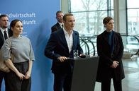 Helix – Wirtschafts- und Umweltminister Bauer (Mitte, Hannes Jaenicke) hält eine umstrittene Rede, seine Personenschützerin Helen Schilling (r., Svenja Jung) und Staatssekretärin Dr. Karlström (l.,Mina Tander) sind über die Reaktionen des Publikums besorgt.