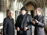 Pfarrer Braun – Bischof Hemmelrath (Hans-Michael Rehberg, links) und sein Adlatus Mühlich (Gilbert von Sohlern, rechts) nötigen Pfarrer Braun (Ottfried Fischer) das Gelübde ab, nie wieder zu kriminalisieren.