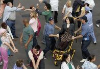 Scrubs - Die Anfänger – Eine Frau (Stephanie D'Abruzzo, liegend) fällt in Ohnmacht. Als sie wieder erwacht, hört sie sich und alle anderen, einschließlich der Belegschaft des Sacred Heart, singen.