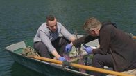 Katastrophen der Erdgeschichte – Die beiden Biologen Patrick Jung und Michael Lakatos untersuchen den Sauerstoffgehalt des Wassers im Alatsee in Bayern. Die rosa Färbung des Wassers ist auf uralte Mikroorganismen zurückzuführen, die in den sauerstofffreien Tiefen des Sees leben.