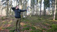 pur+ – Moderator Eric Mayer steht mit seinem Bogen im Wald und zielt zwischen den Bäumen auf eine Zielscheibe. Er lernt innerhalb eines Tages, mit einem modernen Compoundbogen zu schießen.