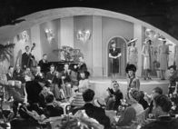 Fräulein Huser – Fräulein Huser Modeschau: Szenenfoto (vorne Mitte - von hinten - Alfred Lohner als Peter Frank, Margarehte Schell-Noé als Mutter Frank)