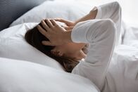 Visite (ARD-alpha) – Nahaufnahme einer Frau, die im Bett liegt, ihren Kopf berührt und sich müde fühlt. Schlaflosigkeit, Schlafstörung, persönliche Probleme, Migräne, Kopfschmerzen.