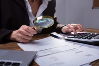 Das System Tönnies – Stockfotografie Geschäftsmann analysiert Rechnung im Büro mit der Lupe
