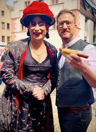 So isst ... – Auf dem Freiburger Münstermarkt ist Sören Anders (re.) mit Dragqueen und Stadtführerin Betty BBQ unterwegs und probiert die legendäre "Lange Rote im Weckle".