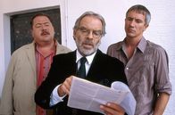 Die Rosenheim-Cops – Harry Prinz (Thomas Fritsch, mi) kann den Cops Hofer (Josef Hannesschläger) und Satori (Markus Böker, re.) mit seinen Unterlagen beweisen, dass alle Verdächtigungen gegen ihn böse Unterstellung sind.