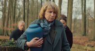 Sterben – Lissy Lunies (Corinna Harfouch) trägt bei einer Beisetzung die Urne mit der Asche ihres Mannes durch einen Wald.