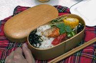 Stadt Land Kunst – Eingelegtes Gemüse, gekochter Mais, Rettichstängel mit Sesam und Lachsscheiben werden für das Bento auf dem gekochten Reis verteilt.