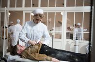 Charité – Schwester Christel (Frida-Lovisa Hamann, r.) schneidet das Hemd eines verletzen Jungen auf.