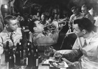Verdammt in alle Ewigkeit – Obwohl Krieg herrscht, ist es auf der Basis der amerikanischen Streitkräfte auf Hawaii noch ruhig. Die Soldaten vergnügen sich im Mannschaftlokal mit Musik. Robert E. Lee Prewitt (Montgomery Clift, vordere Reihe Mitte) spielt Trompete, sein Freund Angelo Maggio (Frank Sinatra, rechts) hört zu. (Darsteller in der vorderen Reihe links: nicht bekannt.)