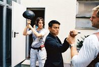 Mit Herz und Handschellen – Wan Kwon (Maverick Queck, M.) bedroht Leo (Henning Baum, r.) mit einem Messer. Nina (Elena Uhlig, l.) setzt den Angreifer elegant mit einer Bratpfanne schachmatt ...