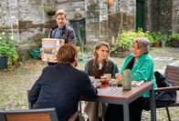 Beyond Paradise – Humphrey (Kris Marshall, im Vordergrund) trifft sich mit Martha (Sally Bretton, 2.v.r.) und deren Mutter Anne (Barbara Flynn, r.) im neu eröffneten Café. Archie (Jamie Bamber, l.) bringt gerade eine neue Weinlieferung.
