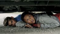 Trio – Nora (Naomi Hasselberg Thorsrud) und Simon (Oskar Lindquist) verstecken sich unter Tom und Julias Geländewagen.