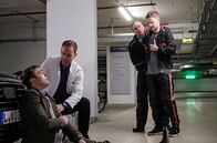 In aller Freundschaft – Als Dr. Kai Hoffmann (Julian Weigend, 2.v.li.) und der Polizist (Komparse) in der Tiefgarage eintreffen, sitzt Gesundheitsdezernent Dr. Clemens Seidel (Moritz von Zeddelmann, li.) zusammengesunken vor seinem Auto. Der Polizist nimmt den Strafgefangenen Dennis Karow (Ilja Roßbander, re.) sofort wieder in Gewahrsam.