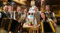 Servus Musikantenstammtisch – Moderator Richard Deutinger (vorne links) posieren für ein Foto mit Tauernwind (hinten).