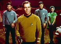 Raumschiff Enterprise – Captain Kirk (William Shatner, M.), Dr. McCoy (DeForest Kelly, l.), Mr. Spock (Leonard Nimoy, 2.v.r.) und die Föderationsbeauftragte Nancy Hedford (Elinor Donahue, r.) sind auf einem unbekannten Planeten notgelandet. Merkwürdigerweise werden sie von einem jungen Mann begeistert empfangen...