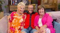 Wohnzimmer-Comedy – Doris Reichenauer, Heinrich Del Core und Petra Binder sitzen gemeinsam im Wohnzimmer auf einer Couch.