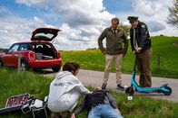 Hubert ohne Staller – Während Riedl (Paul Sedlmeir, r.) mit den Überresten des E-Rollers kämpft, schaut sich Dr. Fuchs (Susu Padotzke, l.) den Toten (Komparse) etwas genauer an. Hat Hubert (Christian Tramitz, M.) den Mann auf dem Gewissen?