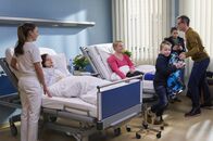In aller Freundschaft – Jessika Wendel (Isabel Bongard, 2. von links) wird von Oberschwester Arzu (Arzu Bazman, links) auf ihr Zimmer gebracht. Dieses teilt sie sich mit Vollblutmutter Silke Bluhm (Floriane Daniel, 4. von rechts), die gerade Besuch ihres Mannes Thomas (Tobias Schulze) und ihrer Kinder hat. Arzu bittet die Rasselbande nun zu gehen, da Jessika jetzt Ruhe brauche.