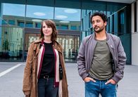SOKO Potsdam – Luna Kunath (Caroline Erikson, l.) und David Grünbaum (Omar El-Saeidi, r.) stehen vor dem Gebäude der "Global Vegan Industries". Das Mordopfer hatte vor ihrem Tod ein Rezept für eine vegane Rübenwurst in Höhe von 500 000 Euro an das Unternehmen verkauft.