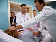 In aller Freundschaft – Brigitte Kiesert (Franziska Trögner, liegend) hat nach dem Streit mit Tom Peters (Volker Lechtenbrink, links) empört sein Zimmer verlassen und ist in ihrer Aufregung gegen ein Krankenbett gelaufen. Schwester Yvonne (Maren Gilzer, 2. von rechts) hat sofort Dr. Roland Heilmann (Thomas Rühmann, 2. von links) und Dr. Martin Stein (Bernhard Bettermann) informiert. Brigittes Leberhämatom ist rupturiert - sie muss notoperiert werden. Tom Peters, der sich verantwortlich fühlt, bleibt betroffen zurück.