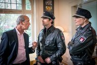 Notruf Hafenkante – Mattes (Matthias Schloo, M.) und Melanie (Sanna Englund, r.) statten dem Betreiber des Flüchtlingsheims, Max Gericke (Thomas Bestvater, l.), einen Besuch ab. Gericke behauptet, zum Zeitpunkt von Bassams Sturz zu Hause beim Frühstück gewesen zu sein, allein.