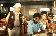 Convoy – Der unsympathische und gemeine Sheriff Wallace (Ernest Borgnine, l.) schikaniert 'Spider Mike' (Franklin Alaye, 2.v.l.), Melissa (Ali MacGraw, 2.v.r.) und 'Pig Pen' (Burt Young, r.) bis aufs Blut ...