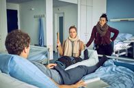 Die Heiland - Wir sind Anwalt – Romy Heiland (Lisa Martinek, M.) und ihre Assistentin Ada Holländer (Anna Fischer, r.) befragen den verletzten SEK-Auszubildenden Mike Neidhard (Sebastian Kaufmane, l.) im Krankenhaus