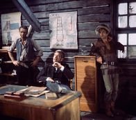 Winnetou 2 – Der Ganove Forrester (Anthony Steel, M.) lässt sich über die Lage informieren. Besondere Aufträge vergibt er an seinen Vertrauten Luca (Klaus Kinski, r.).