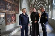 WaPo Bodensee – Paul Schott (Tim Wilde, r.) und Nele Fehrenbach (Floriane Daniel, l.) treffen Abt Barnabas (Ulrich Gebauer, M.) im Kreuzgang von Kloster Oberzell.